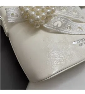 Dettaglio della trama in pelle bianca con cuore di perle e nastro di pizzo su una borsa