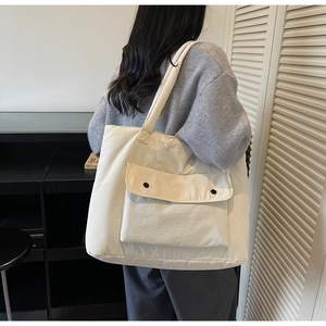 Minimalist beige canvas tote bag detail showing the front pocket with black button closure