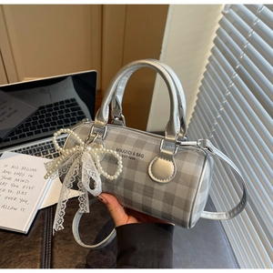 Détail du sac cylindre à carreaux argenté avec nœud en perles et breloque dentelle