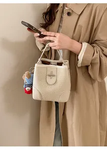 Detail of beige lychee pattern bucket bag with silver buckle and bear charm on trench coat