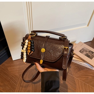 Détail d'un sac bandoulière vintage marron foncé avec finition cirée et perles en bois