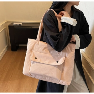 Detail of light pink nylon tote bag showing front flap pocket and textured fabric finish