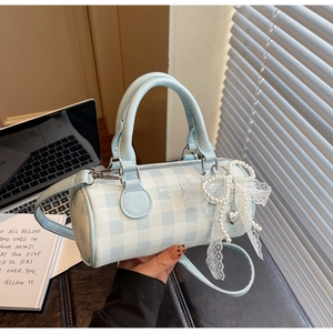 Détail d'un sac cylindrique à carreaux bleu clair avec nœud en dentelle de perles et cœur