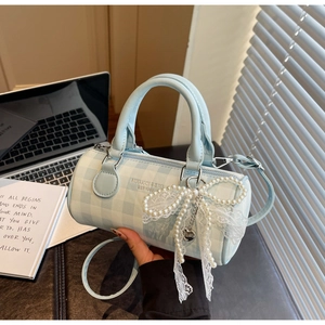 Détail du sac Boston à damier bleu avec perle et nœud en dentelle sur un bureau