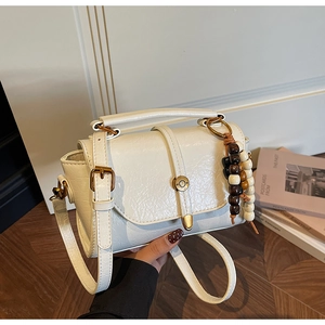 Détail du sac bandoulière en similicuir blanc avec boucle dorée et perles en bois