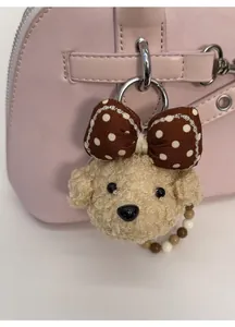 Detail of beige teddy plush pendant with polka dot bow attached to a pink handbag