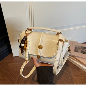 Détail du sac bandoulière crème avec fermoir bronze vintage et breloque en perles de bois