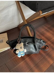 Detail of black bucket bag with matte texture, shoulder strap and cute plush bear charm