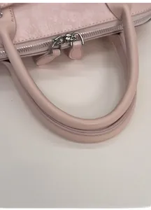 Detail of pink textured leather handbag showing sturdy round handles and silver zippers