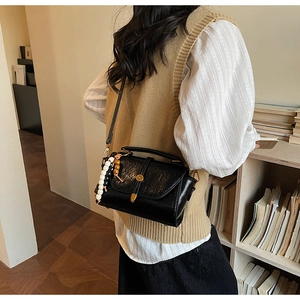 Détail du sac bandoulière en cuir ciré noir avec fermoir doré et sangle perlée