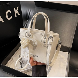 Detail einer cremefarbenen Beuteltasche mit Perlenherz-Anhänger in einer Geschenkbox