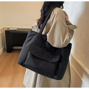 Detail of black nylon tote bag featuring front flap pocket and metal snap buttons