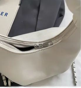 Detailed macro view of smooth silver metal zipper and chain strap on cream dumpling bag