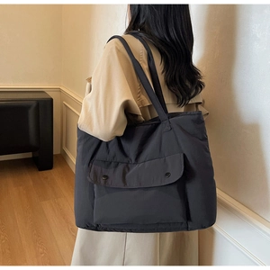 Rear view of a model wearing a large black quilted tote bag with double front pocket flaps