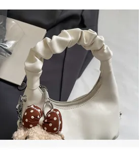 Close-up of cream crescent bag with pleated handle, brown bow, and plush bear charm detail