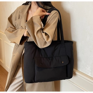 Detail of large black canvas tote bag showing front pocket and metal buttons on shoulder strap