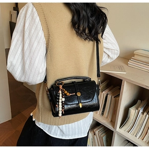 Détail du sac bandoulière noir en similicuir avec pompon en perles de bois et texture vintage