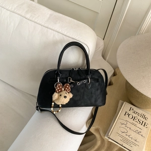 Detail of matte black vintage Boston bag with a cute bear pendant on a soft sofa