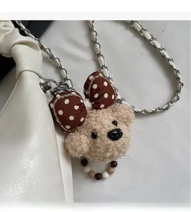 Close-up of beige plush bear charm with polka dot bow and beads on a white bag