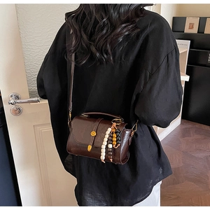 Détail du petit sac bandoulière vintage marron avec sangle perlée porté par un modèle