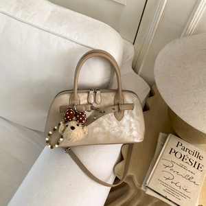 Beige matte leather crossbody bag with teddy bear charm on a minimalist white sofa