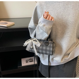 Détail du sac cylindrique à carreaux gris avec nœud en dentelle et pendentif perle