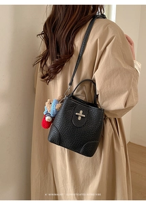 Litchi texture bucket bag with woven teddy bear charm worn by model in trench coat