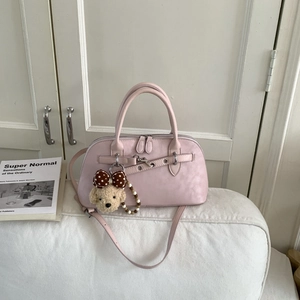 Detail of light pink doctor-style handbag with dog plush charm on a white sofa