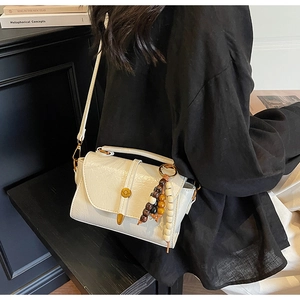Vue détaillée d'un sac à bandoulière en cuir crème avec pompon perlé et boucle en métal