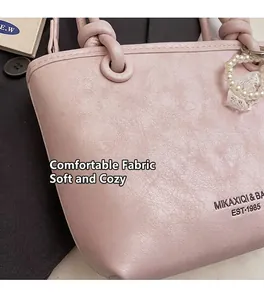 Détail du sac seau en cuir rose avec poignée nouée et breloque perle en cœur