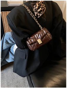 Detail of dark brown quilted crossbody bag with gold chain strap on a black blazer