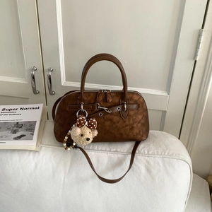 Detail of dark brown retro tote bag with matte texture, silver rings and bear charm