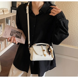 Détail du sac bandoulière blanc avec texture litchi et accessoire de gland à perles