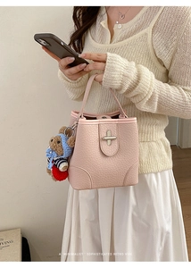 Detail of pink lychee leather bucket bag featuring a gold twist lock and plush bear charm