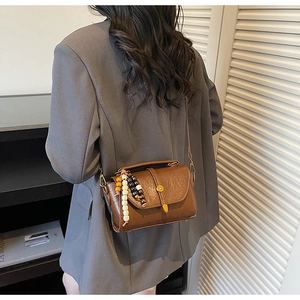 Gros plan du sac bandoulière en cuir marron texturé avec breloque en perles bois