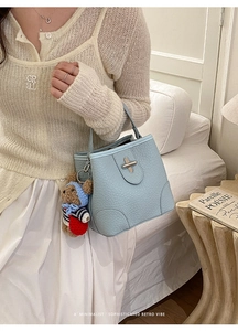 Detail of light blue lychee pattern leather bucket bag with a cute bear charm accessory