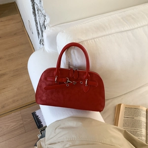 Detail of dark red frosted leather handbag with silver metal buckles on a white sofa