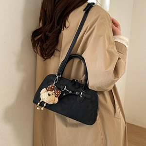 Close-up of black matte Boston bag with silver hardware and plush bear charm on beige coat