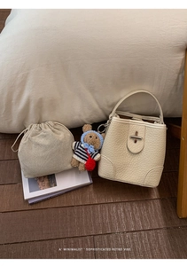 Detail of a white bucket bag with pebble leather texture, silver lock, and a bear charm