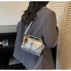 Détail de la texture argentée du sac carré et du charme perlé porté par le mannequin