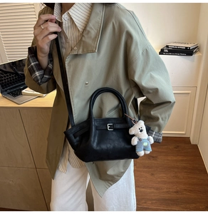 Detail of black pleated bucket bag with leather strap and white teddy bear charm