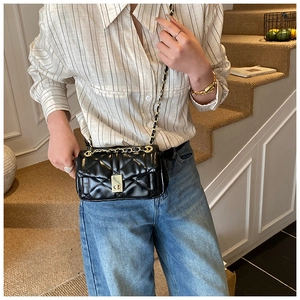 Detail of black quilted chain bag with gold metal clasp on a stylish shoulder strap
