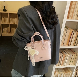 Rosa Eimertasche schräg getragen mit Details einer Spitzenschleife und Perlenherz-Anhänger