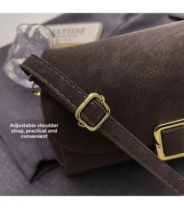 Detail of adjustable shoulder strap with gold buckle and white stitching on brown bag