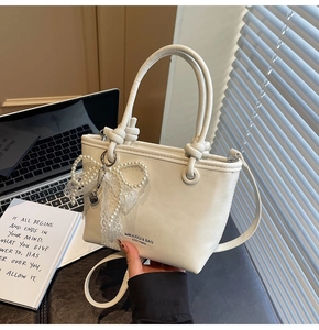 Détail du sac seau blanc avec pendentif nœud en dentelle et perles et poignée nouée