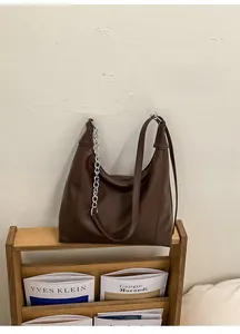 Detail of dark brown faux leather tote with vintage silver chain on a magazine rack