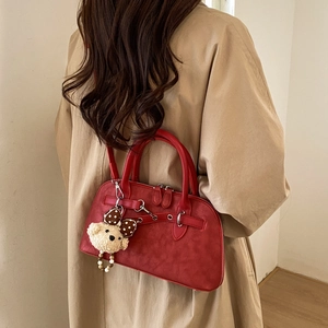 Close-up of a red matte leather Boston bag with plush bear charm on beige trench coat