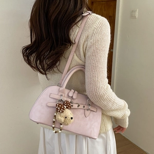 Detail of pink suede shell bag with teddy bear charm shown on a model in knitwear