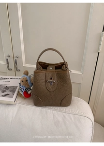 Detail of tan pebbled leather bucket bag with silver clasp and cute bear charm