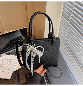 Gros plan d'un sac seau noir avec nœud en dentelle perlée et décor de bureau